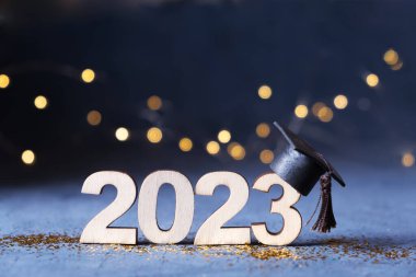 Class of 2023 concept. Wooden number 2023 with graduate hat on dark background with bokeh.