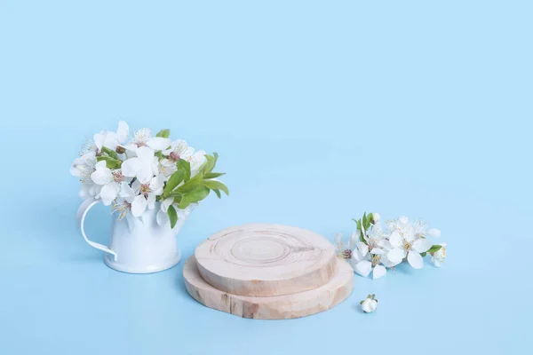 Wooden podium or pedestal with cherry blossoms in a watering can on blue background. Mock up for cosmetic products.