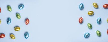 Paskalya Avı konsepti düzdü. Çikolata renkli yumurtalar mavi arkaplanda üstten görünüyor.