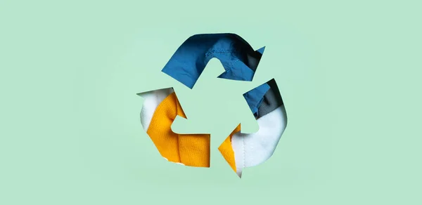 Second hand, clothing donation and recycling concept. Colorful clothes under paper cut recycling symbol.