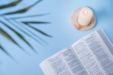 Christian Holy Bible with candles and palm leaves on blue background