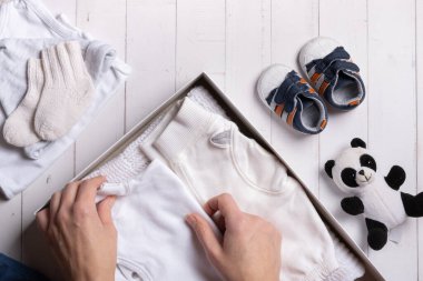 Kadın elleri çocuk kıyafetlerini, ayakkabılarını ve oyuncaklarını bir kutuya koyar. İkinci el, kıyafet geri dönüşüm konsepti.