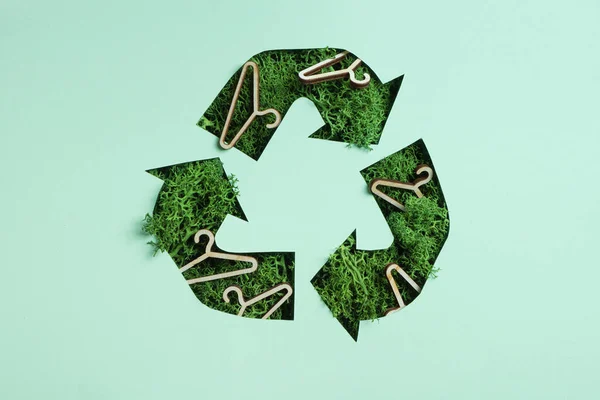 Green moss and coat hangers under paper cut recycling symbol. Save planet recycling cloth concept.