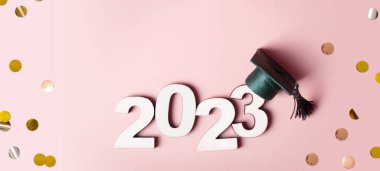 2023 sınıfı konsepti. Ahşap numara 2023, renkli arka planda mezuniyet şapkası var..