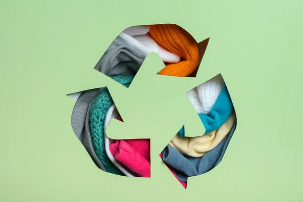 Second hand, circular fashion and recycling concept. Colorful clothes under paper cut recycling symbol.