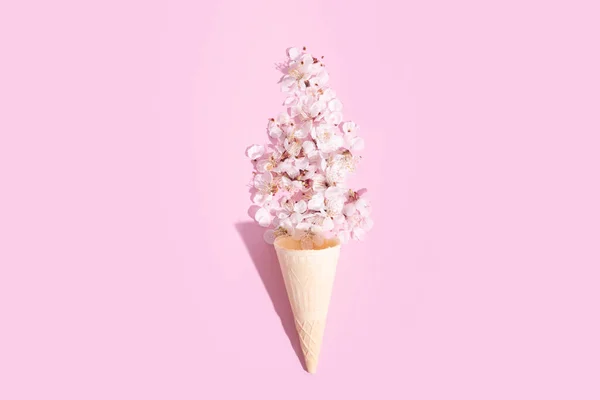 stock image A waffle cone with delicate cherry blossom petals on a pink background. Spring creative photo.