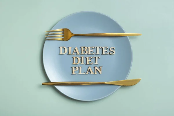 Diabetes diet plan text on plate on colored background with cutlery flat lay, top view.
