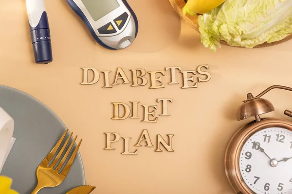 Diabetes diet plan text with plate and cutlery, glucose meter on beige background flat lay, top view.