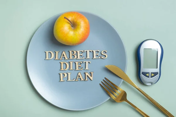 Diabetes diet plan text. A glucometer and a plate with cutlery on colored background flat lay, top view.