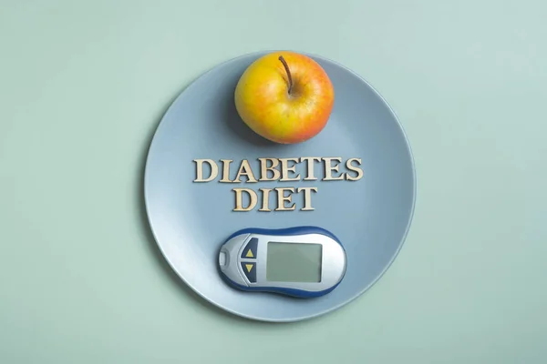 Diabetes Diet Plan text. Glucometer and plate with apple on colored background flat lay, top view.