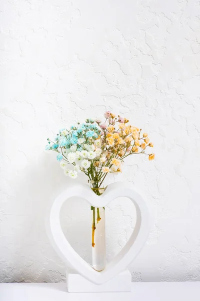 Plaster vase in the shape of a heart with multi-colored gypsophila flowers on white background.