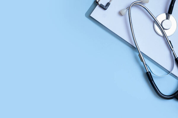 Fragment of stethoscope, tablet on blue background with copy space. Healthcare and medicine concept flat lay, top view.