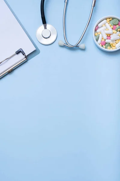 stock image Fragment of stethoscope, tablet, pills on blue background with copy space. Healthcare and medicine concept flat lay, top view.