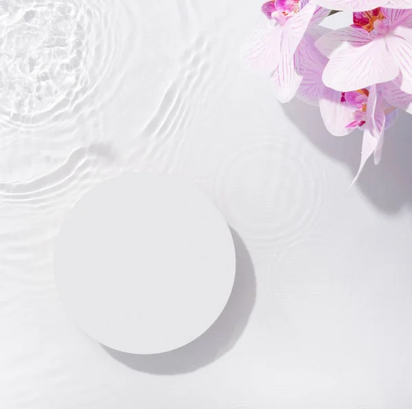 stock image Podium or pedestal of water ripples and orchid flowers lying flat, top view. Summer cosmetic template, mockup.