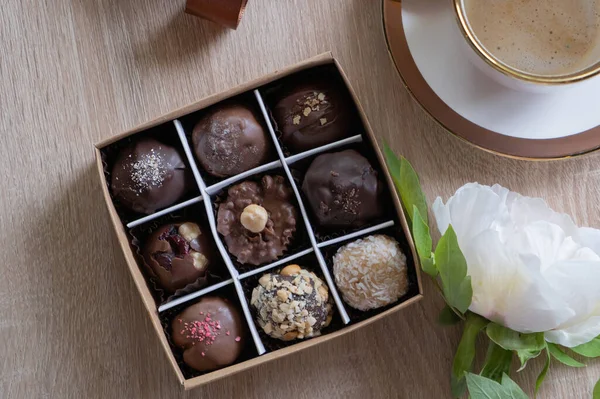 Chocolate craft candies in box with coffee and flower on table top view, flat lay.
