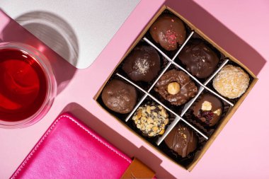 Üzerinde çikolatalı şekerlemeler olan hediye kutusu pembe çalışma masasının arkası düz, üst görünüm.