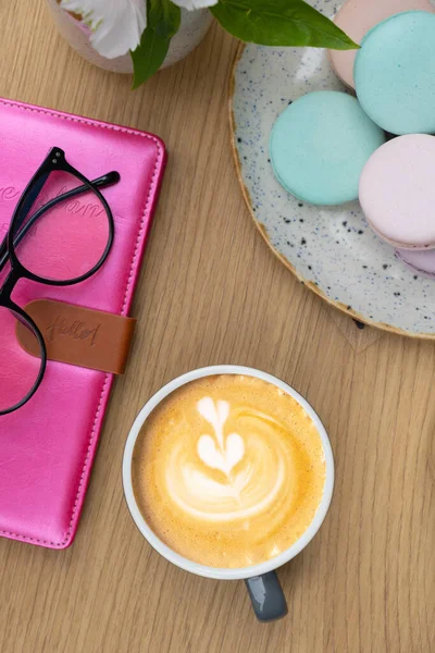 Cup of coffee flat lay with notepad and pastel colors pastry macaroons on a wooden table top view.