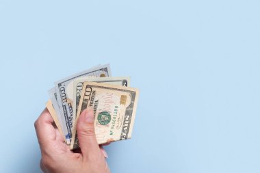 Mavi arka planda kadın eli dolar. Minimalist finansal konsept.