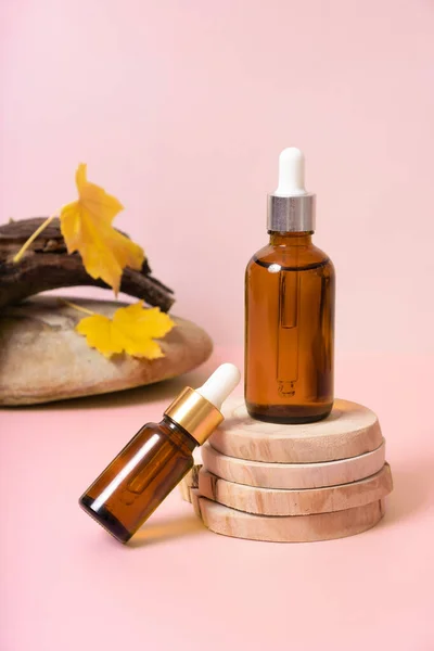 Glass dropper bottles with cosmetics oil or serum at autumn scene composition with podium.