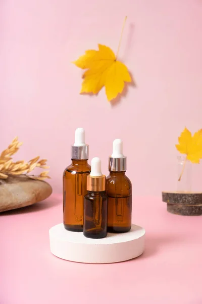 Glass dropper bottles with cosmetics oil or serum at autumn scene composition with podium.