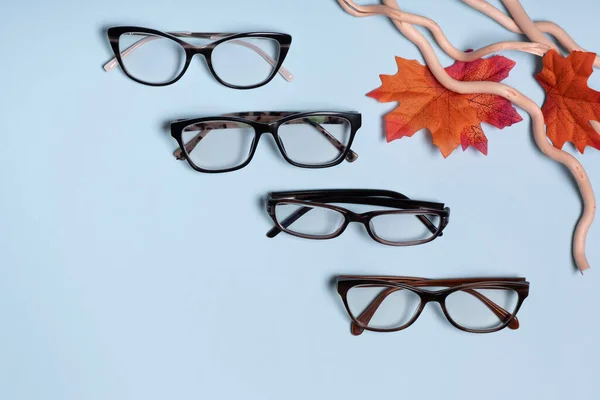 Glasses for vision on a blue background with autumn leaves. Optical store, vision test, stylish glasses concept.
