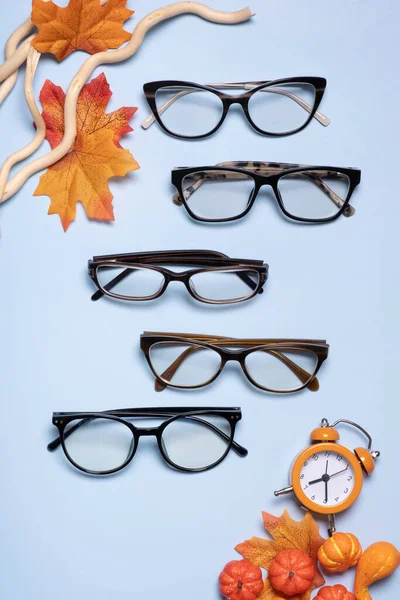 Glasses for vision on a blue background with autumn leaves and pumpkin. Optical store, vision test, stylish glasses concept.