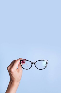 Mavi arka planda kadın eli gözlüklü. Optik mağaza, görüş testi, şık gözlük konsepti.