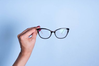 Mavi arka planda kadın eli gözlüklü. Optik mağaza, görüş testi, şık gözlük konsepti.