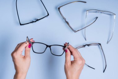 Mavi arka planda kadın eli gözlüklü. Optik mağaza, görüş testi, şık gözlük konsepti.