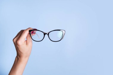 Mavi arka planda kadın eli gözlüklü. Optik mağaza, görüş testi, şık gözlük konsepti.