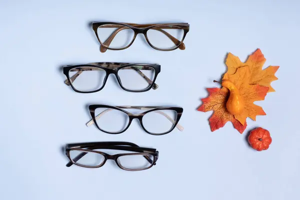 Glasses for vision on a blue background next to autumn leaves and pumpkin. Optical store, vision test, stylish glasses concept.