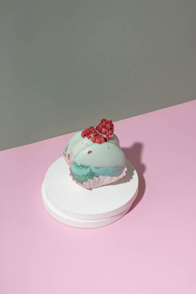 Raspberry-pistachio macaroon on a podium on pastel pink-green background. Delicious food aesthetics