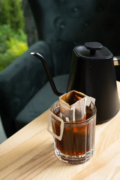 Glass cup with making coffee from drip bag on wooden table. Trends in making coffee at home