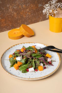 Sebzeli salata, balkabağı, yumuşak peynir ve bej arka planda çatal bıçak takımı.