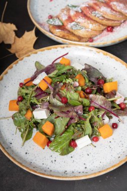 Koyu arkaplanda yeşil salata, kabak ve yumuşak peynir tabağı.