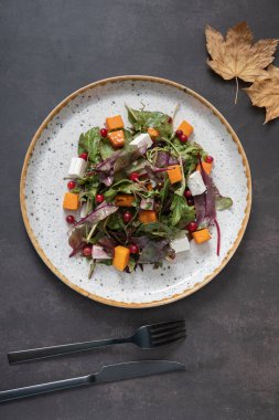 Yeşillikli salata, kabak, yumuşak peynir ve koyu arkaplanda çatal bıçak takımı.