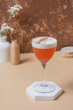 Kürsüde ya da vazolarda kuru çiçekler olan kaidede bulunan saplı camda parlak alkollü kokteyl.