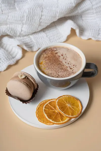 A cup of warm cocoa with a macaroon and cozy winter decor. Winter still life with a warm drink.