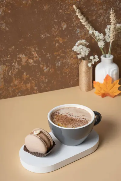 A cup of warm cocoa with a macaroon and cozy autumn decor. Fall still life with a warm drink.