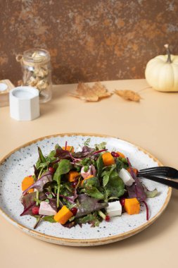 Yeşil salata, balkabağı, yumuşak peynir ve bej arka planda çatal bıçak takımı.