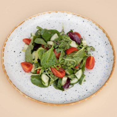 Taze salata roka, kiraz domatesleri bej arka plan manzaralı bir tabakta salatalık.