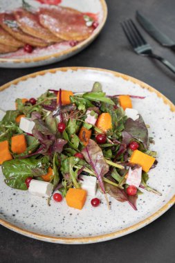 Yeşillikli salata, kabak, yumuşak peynir ve koyu arkaplanda çatal bıçak takımı.