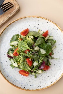 Taze salata roka, kiraz domatesleri, salatalıklar bir tabakta, arka planda bir renk üst görünümü..