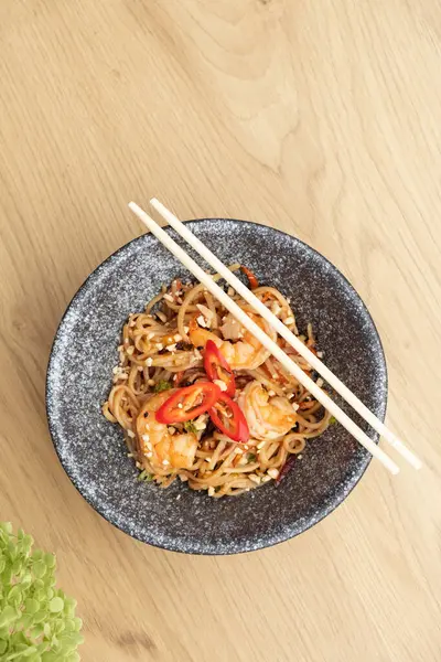 stock image Udon noodles with shrimp and fried vegetables in a bowl top view, flat lay on wooden table.