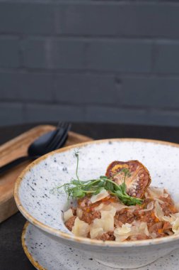 Bolognese in a bowl on a dark background decoration with dry tomato and microgreen.