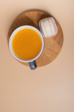 Cup of sea buckthorn tea and macaroon flat lay, top view on beige background.