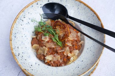 Bolognese in a bowl decorated dry tomato and microgreen on a wooden table top view, flat lay.