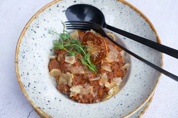Bolognese in a bowl decorated dry tomato and microgreen on a wooden table top view, flat lay.