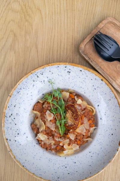 Bolognese in a bowl decorated dry tomato and microgreen on a wooden table top view, flat lay.