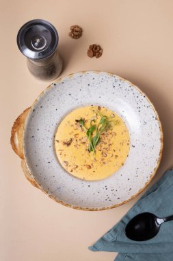 Bir tabak peynirli, fındıklı, yeşillikli ve arka planda bej bir krem çorba.